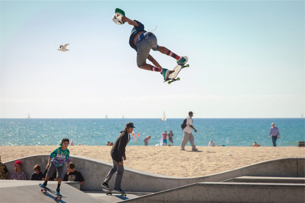 Skateboarder performing a stunt on the beach with an ocean view in the background.